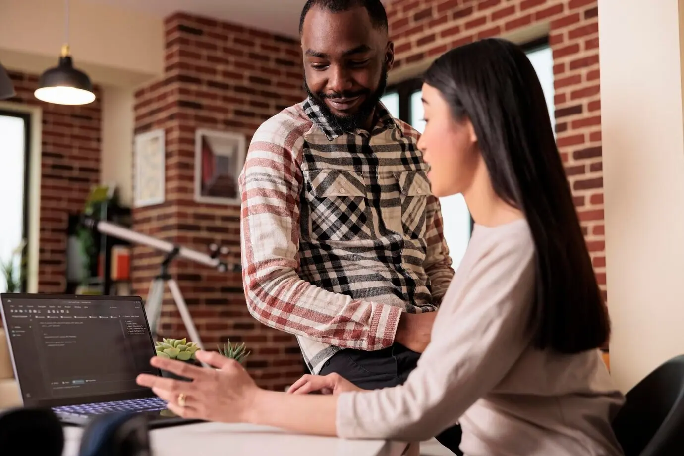 Двое программистов создают код шифрования на ноутбуке, работая в окне терминала с HTML-скриптом и двоичным кодом. Программируют облачный сервер онлайн‑приложения, защищённый брандмауэром.