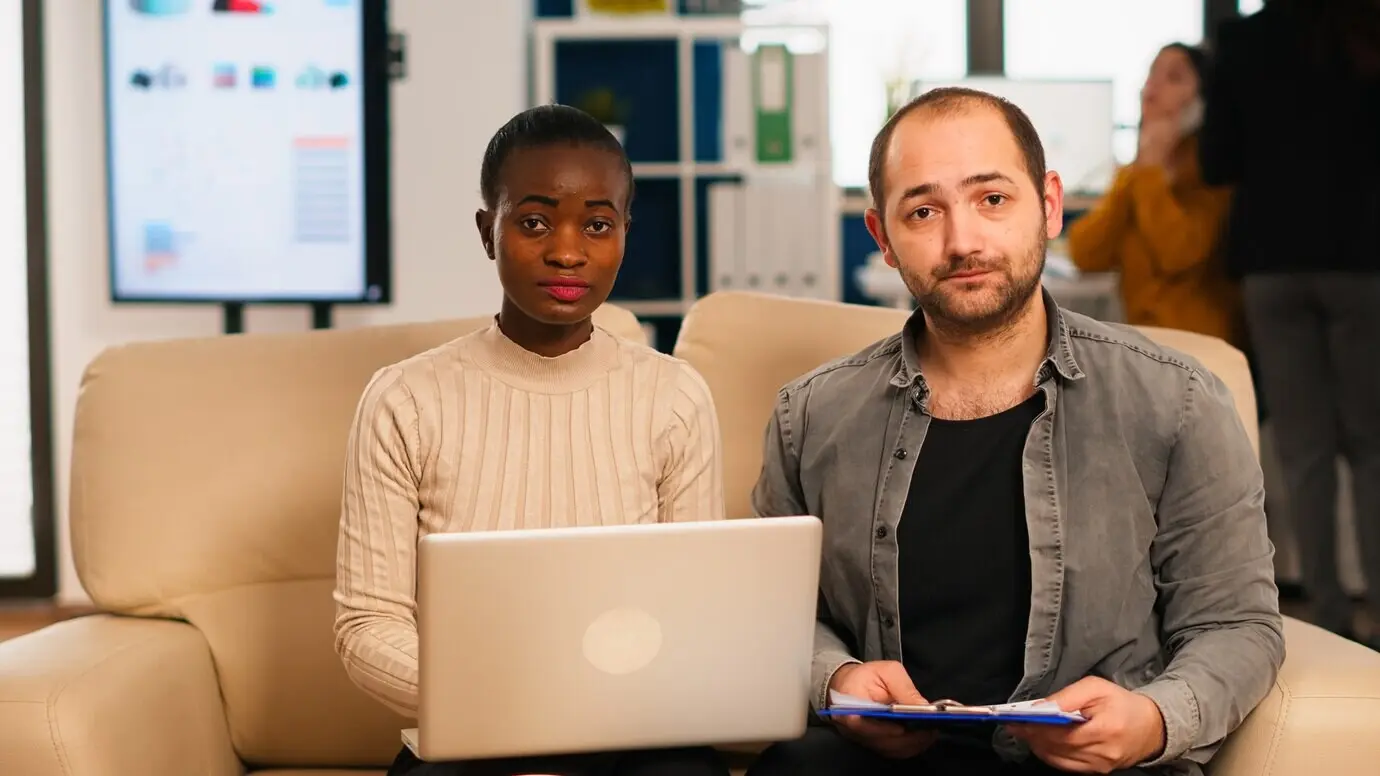 Ракурс от первого лица: разнообразные коллеги, сидя на диване в современном офисе стартапа, обсуждают финансовую стратегию на видеовстрече через веб‑камеру, работая для нового бизнеса. Мультиэтнические сотрудники анализируют ре