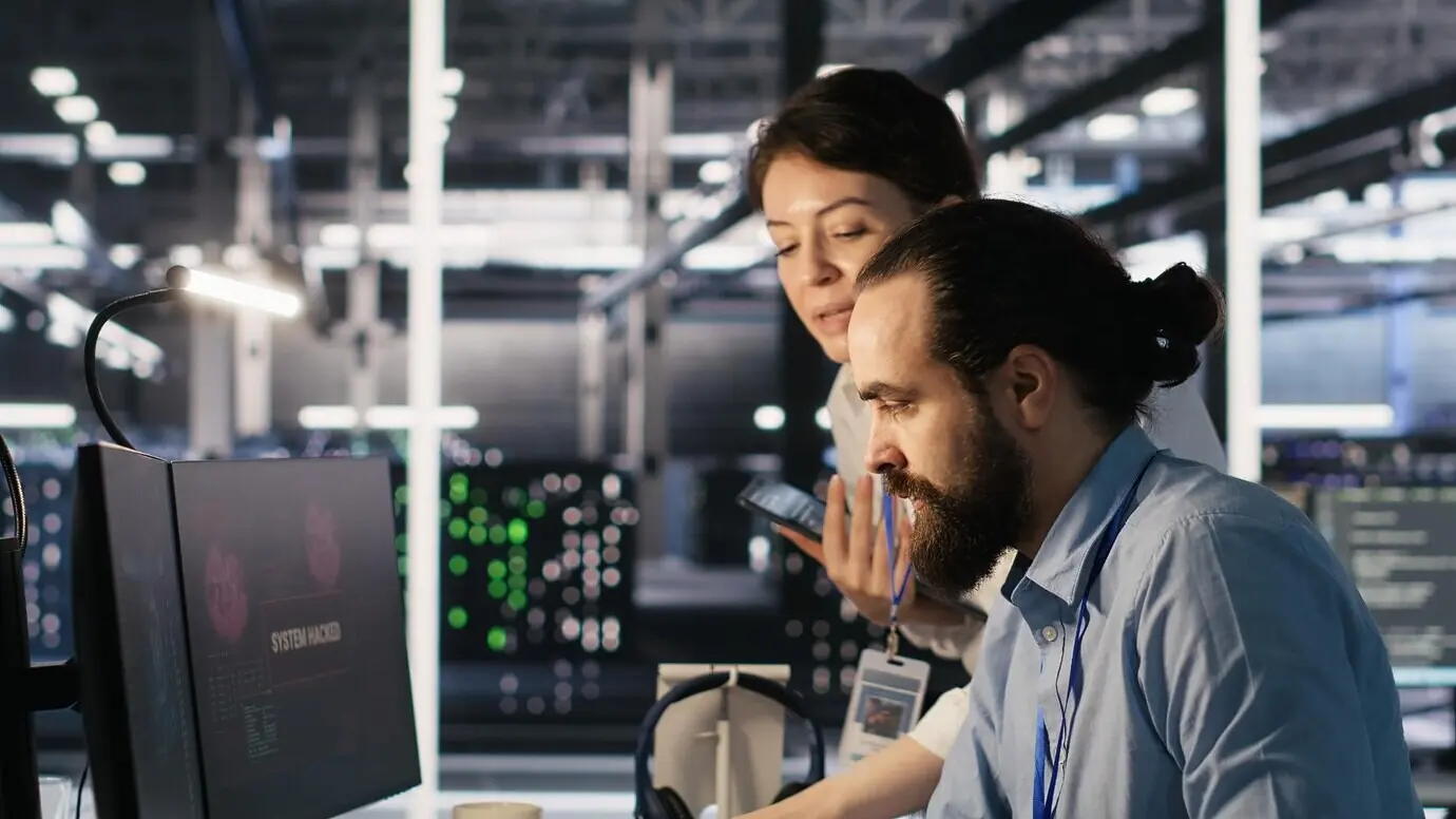 Взволнованные техники в дата-центре реагируют на блокировку системы, вызванную хакером.